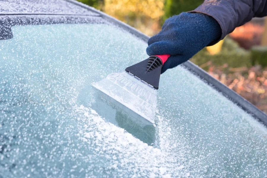 Hand wearing blue glove scratching ice from car window