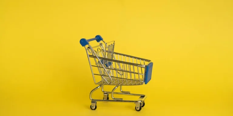 Isolated shining metal shopping trolley without anything located separately on yellow background