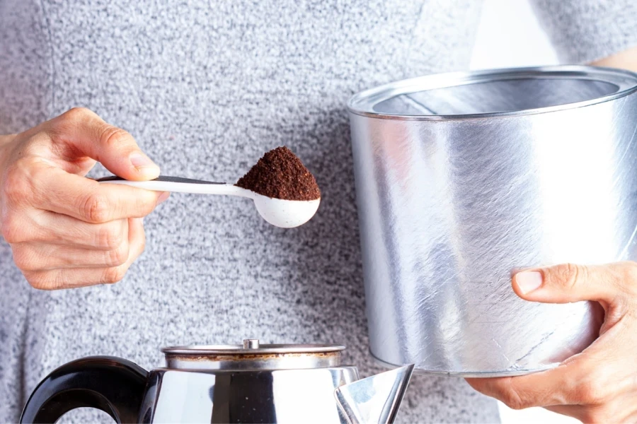 Lady holding a spoonful of coffee beside a percolator