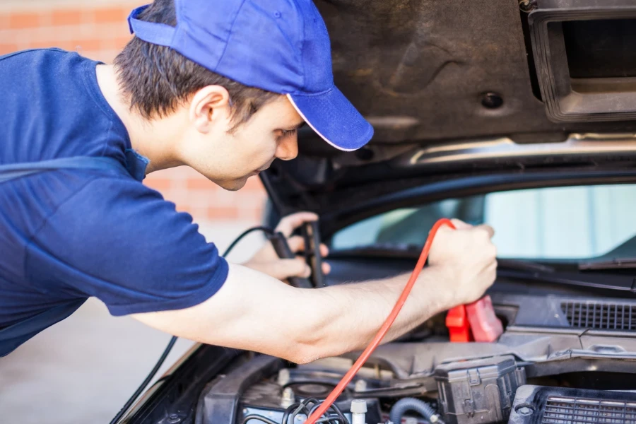 Mechanic using booster cables to start-up a car engine