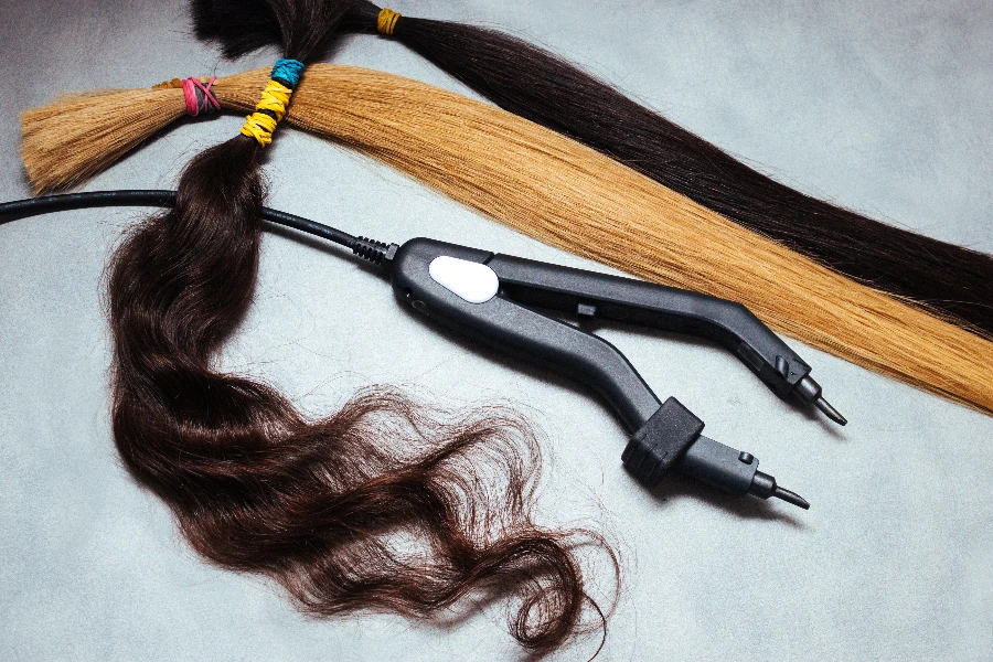 Multicolored hair extensions and tongs close up on gray background