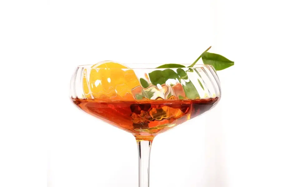 One couple glass filled with a cocktail, fruit, and mint leaf