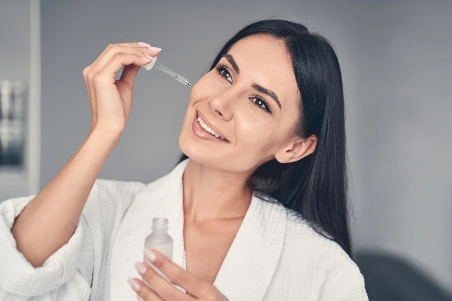 Portrait of a pleased relaxed modern pretty woman applying a facial serum to her skin