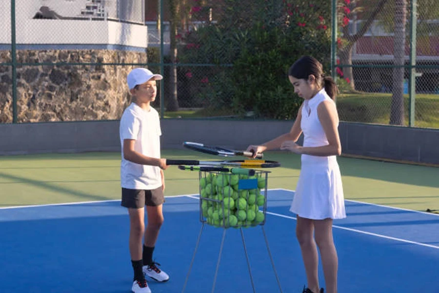 Two tennis players putting balls in a hopper