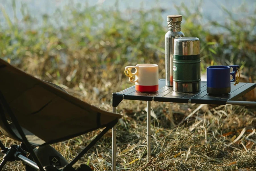 Two vacuum flasks and two cups on a table outdoors