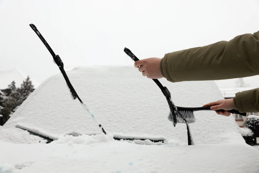 Woman cleaning car wiper blade from snow with brush outdoors