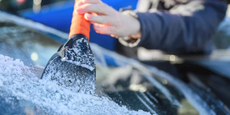 Woman deicing car windshield with ice scraper