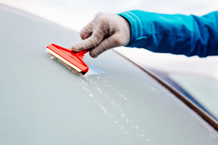 Woman deicing front car windshield with scraper