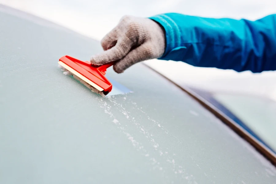 Woman deicing front car windshield with scraper