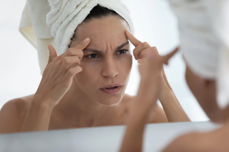 Worried young woman wrapped in towel looking in mirror in bathroom