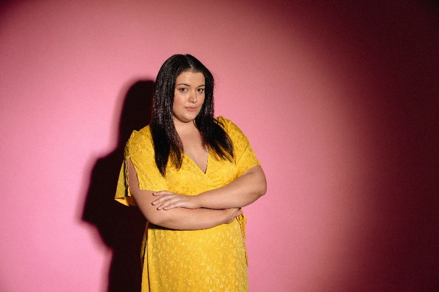 Young female adult standing in front of a pink studio background