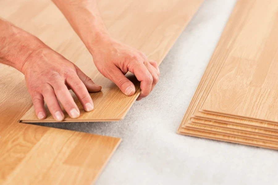 A man's hands laying yellow laminate flooring