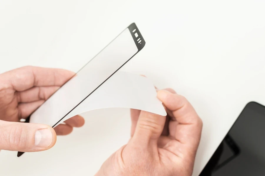 A man is glueing a protective glass on the screen of a smartphone