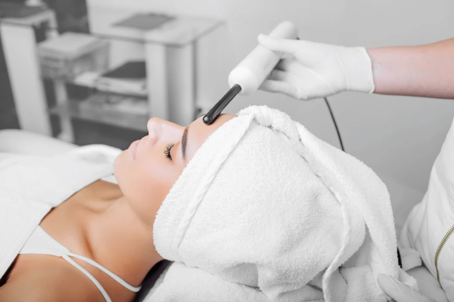 woman getting electric darsonval facial massage procedure at beauty salon
