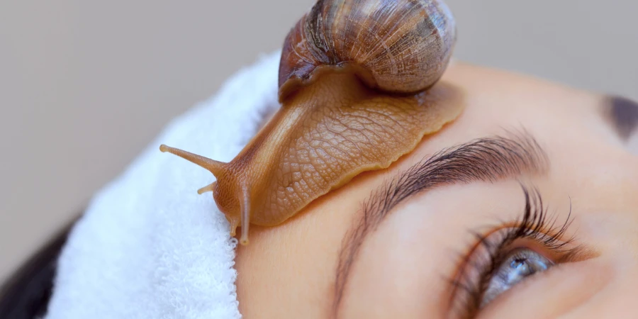 Beautiful young woman with a snail ahatin on her face in a beauty salon