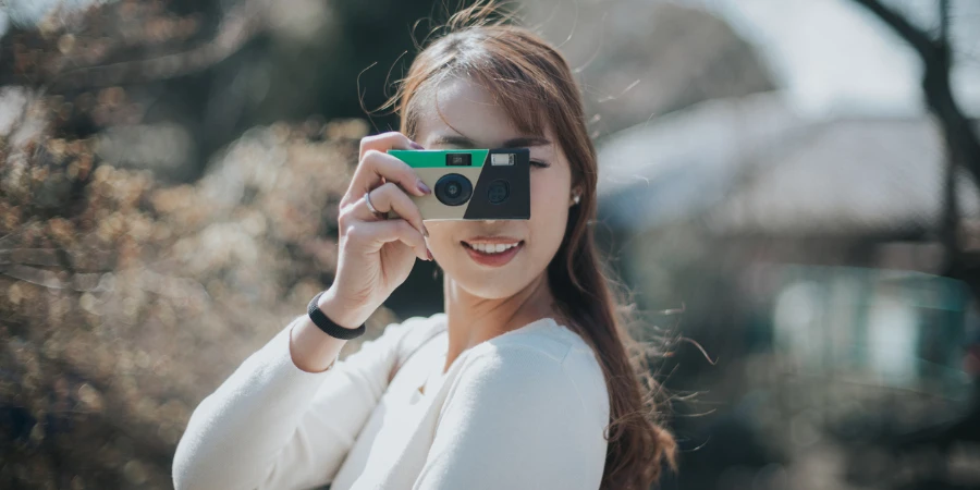 Joyful young woman taking photos with disposable camera