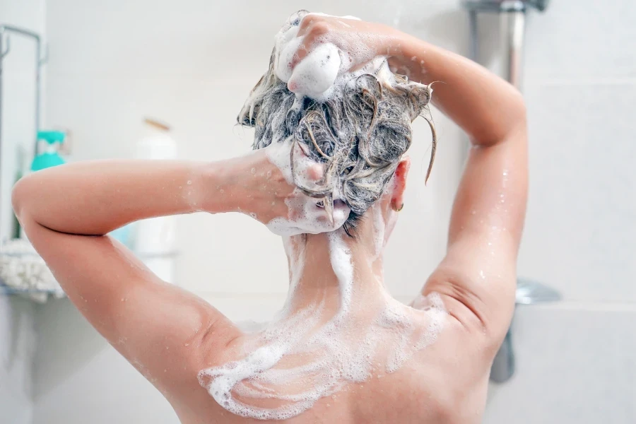 Woman washes her hair with shampoo in bathroom
