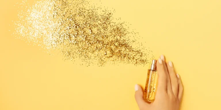 Female hand holding stylish bottle of perfume with spray of sparkles