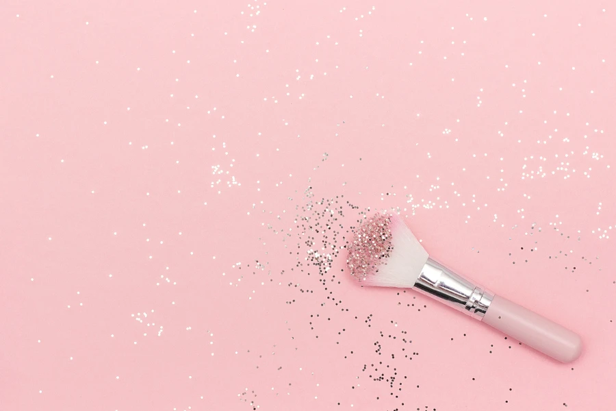 Makeup brush and shiny sparkles on pastel pink background
