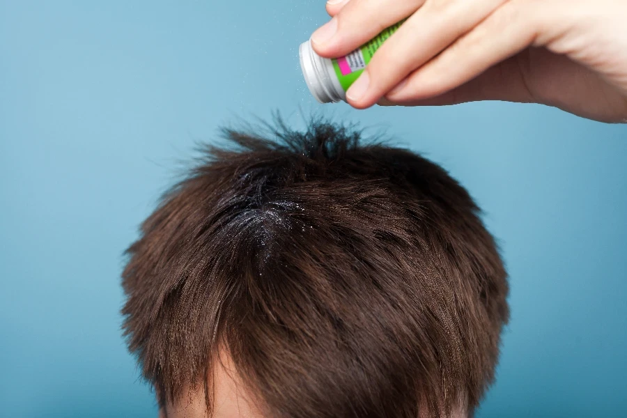 Closeup of male hand applying medications on brunette male hair
