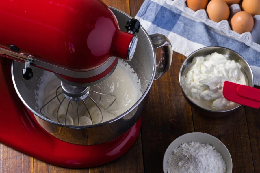 Standing mixer on wooden table with ingredients
