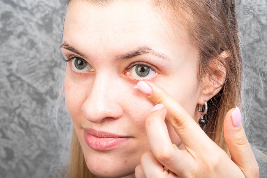 Young attractive woman does morning makeup applying cream around eyes
