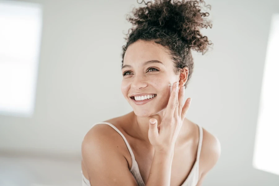 Smiling young women applying moisturiser to her face
