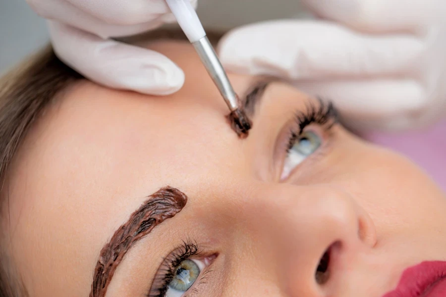 Close-up Photo of Beautician Applying Dye on Woman's Eyebrows
