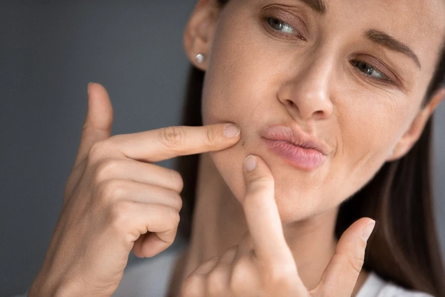 Close up of anxious young woman look in mirror in bathroom squeeze pimple on face