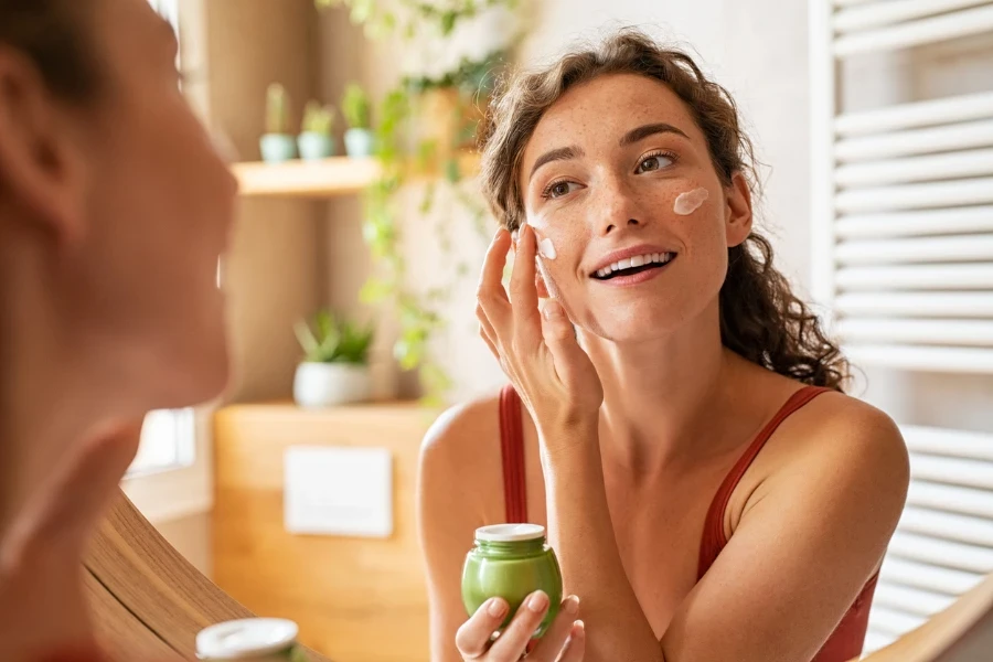 cropped shot of beautiful woman in bathrobe applying face cream