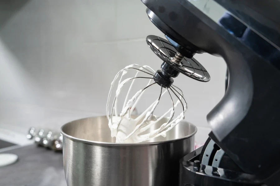 open black Electric stand mixer on a table in the kitchen with white cream
