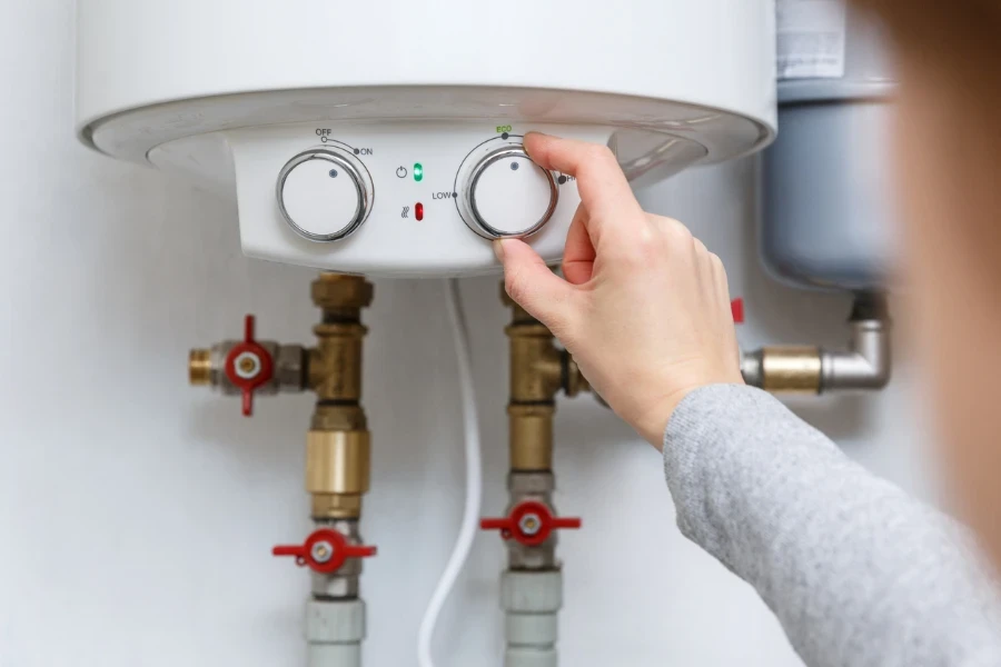 Female hand puts thermostat of electric water heater
