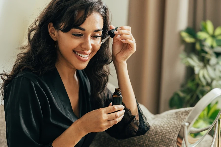 young smiling woman sitting on a couch applying hyaluronic acid on a face
