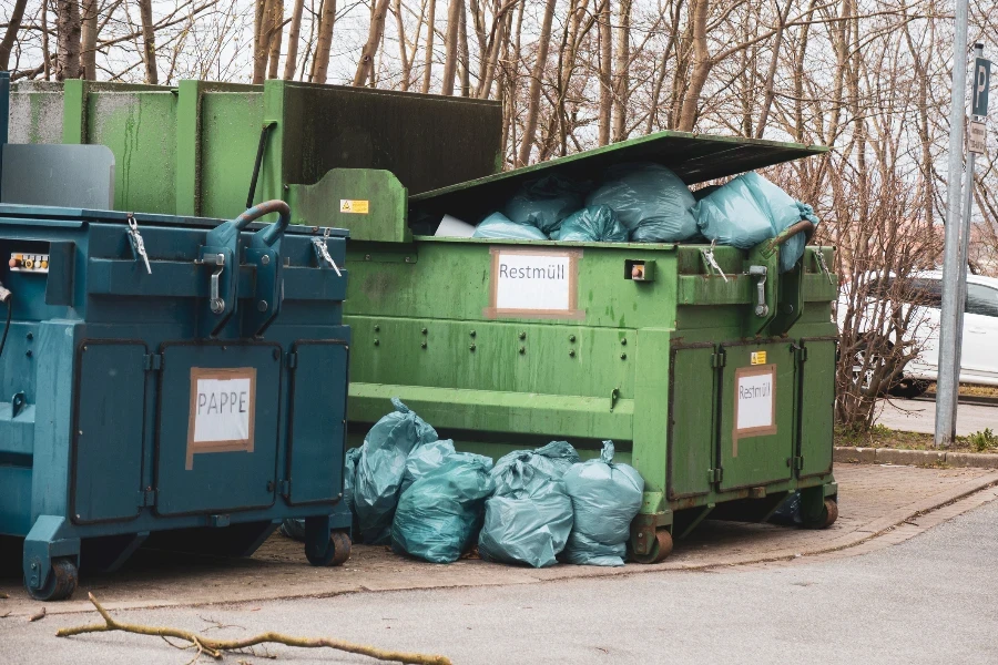 next to two trash compactors are numerous blue trash bags
