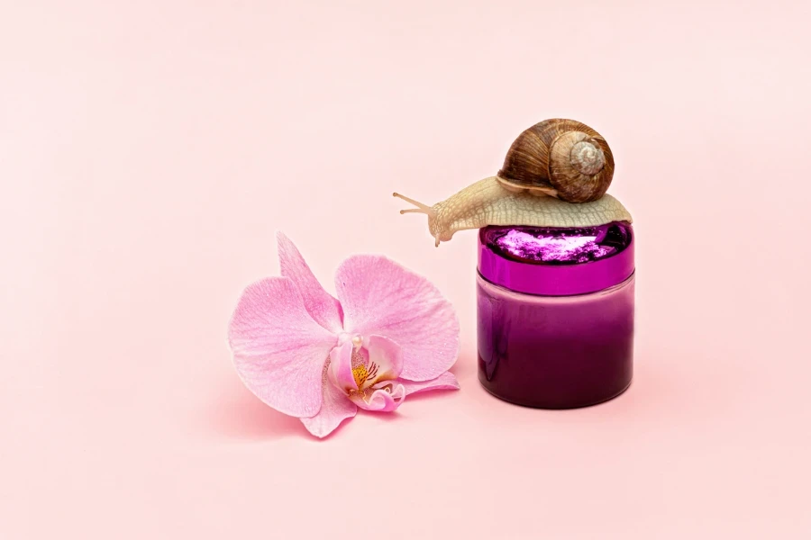 Skin rejuvenation cosmetics on pink background with snail and orchid flower
