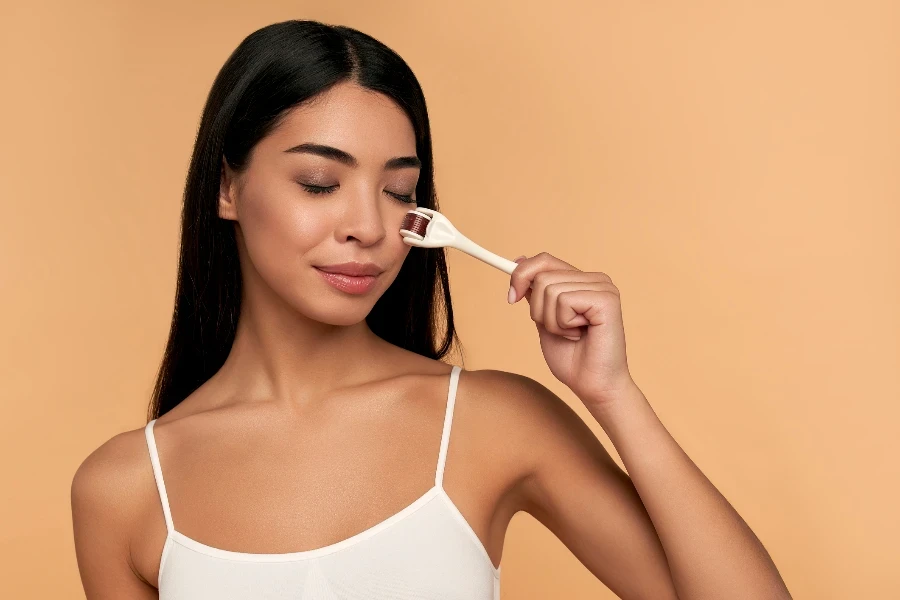 Close-up of Asian female face with derma roller for mesotherapy procedures
