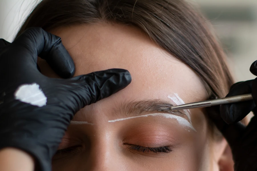 Young woman undergoing eyebrow correction procedure in beauty salon

