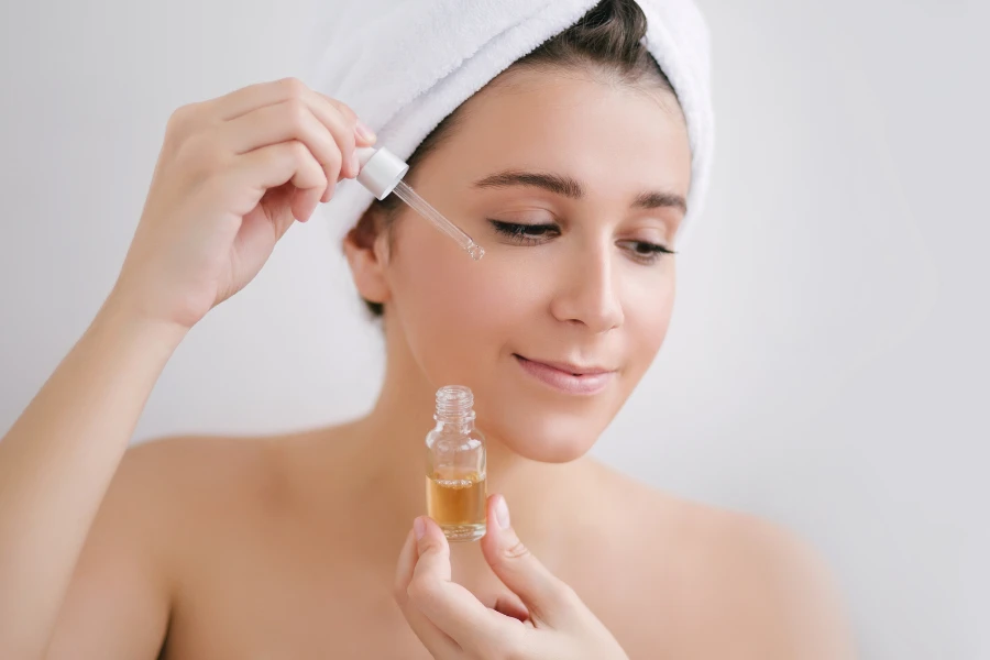 Portrait of beautiful young woman with towel on head holding face oil
