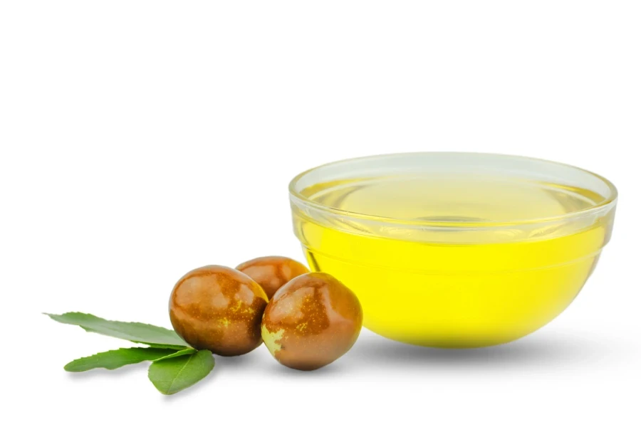 Bowl with jojoba oil and ripe fruits on white background
