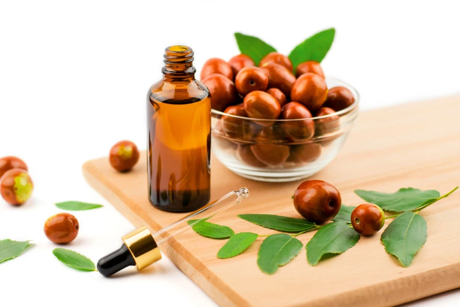 Jojoba oil in a bottle with a dropper on a wooden table with ripe jojoba fruits
