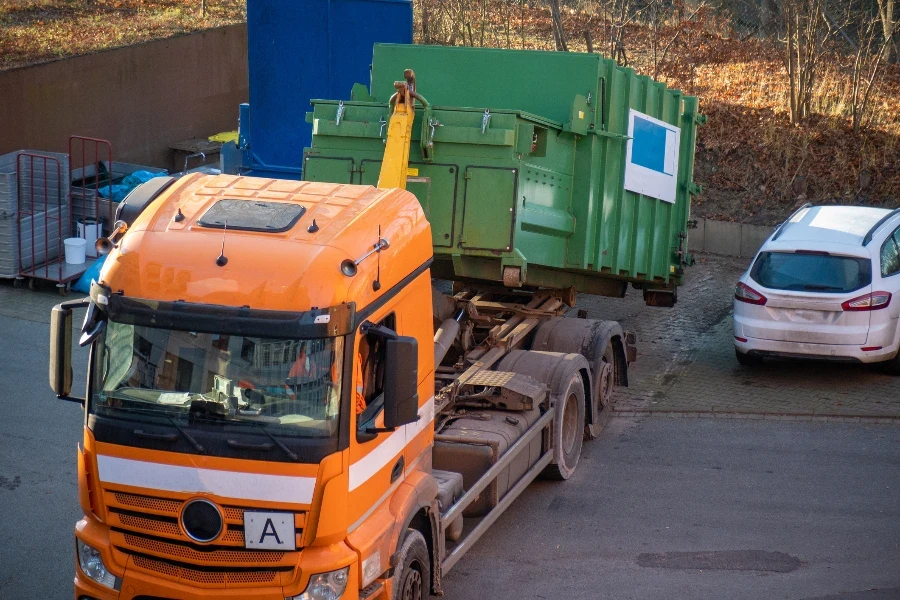 an orange truck drops off a trash compactor in the yard of a hospital
