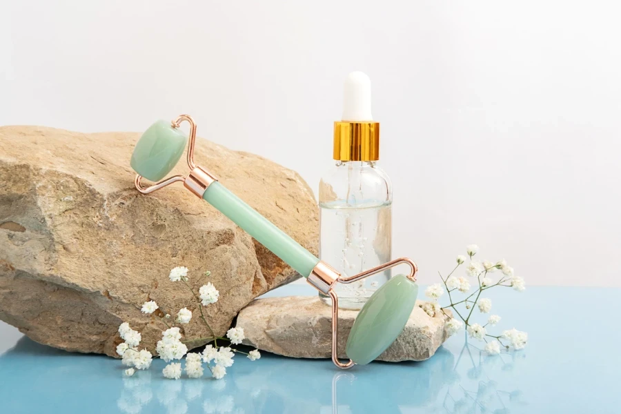 Green jade roller facial massager gouache and cosmetic bottle on stones
