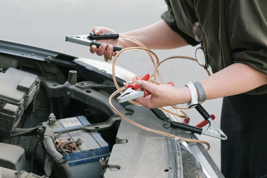 a car with the hood open and holds the battery charging clamps