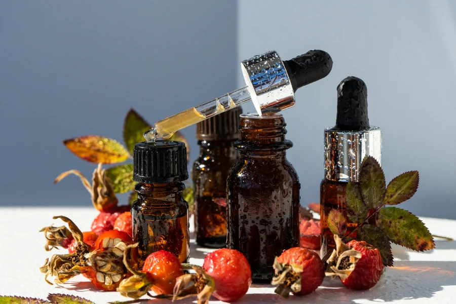 Bottles of essential oil and ripe rose hip berries on white background
