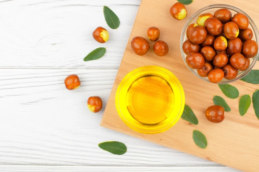 Fresh ripe jojoba fruit and jojoba oil in bowl on wooden table
