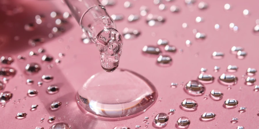 Pipette, drop and splashes of micellar water on a pink background