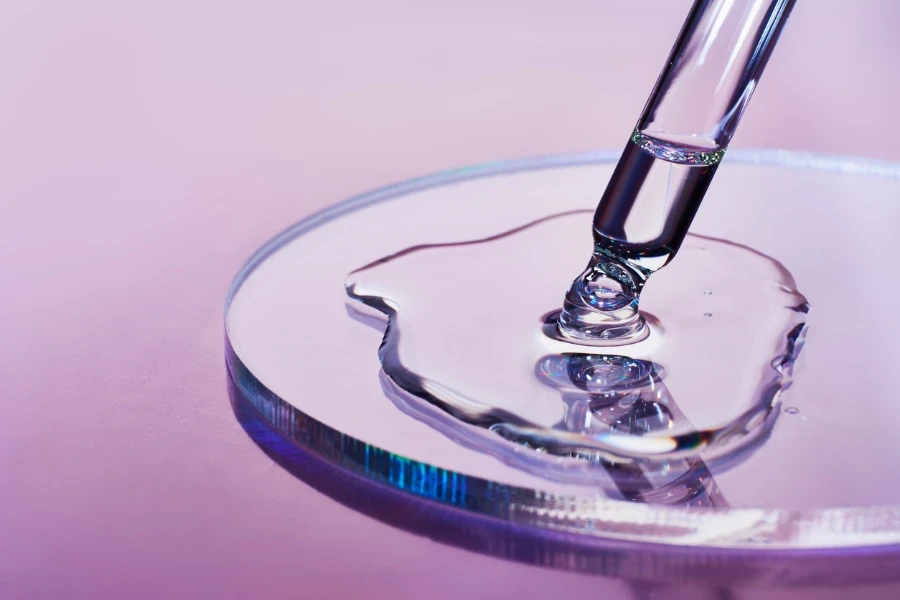 Pipette with sample of cosmetic product in petri dish on holographic background
