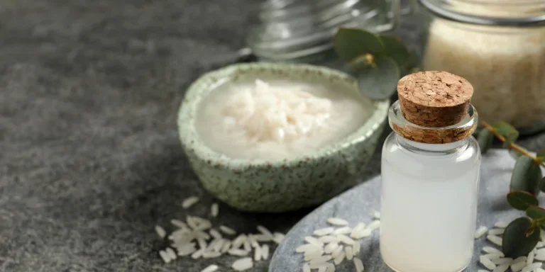 Glass bottle with rice water and grains on grey table.