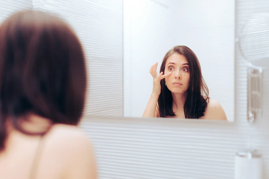 Girl correcting her dark circles and puffy eyes with concealer makeup product
