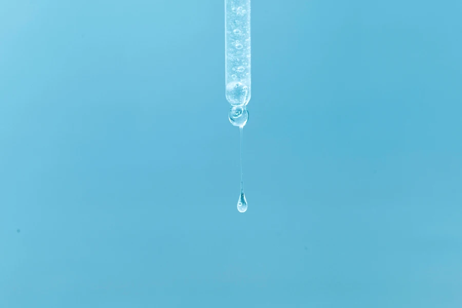 Cosmetic pipette with a transparent drop of serum close-up on a blue background
